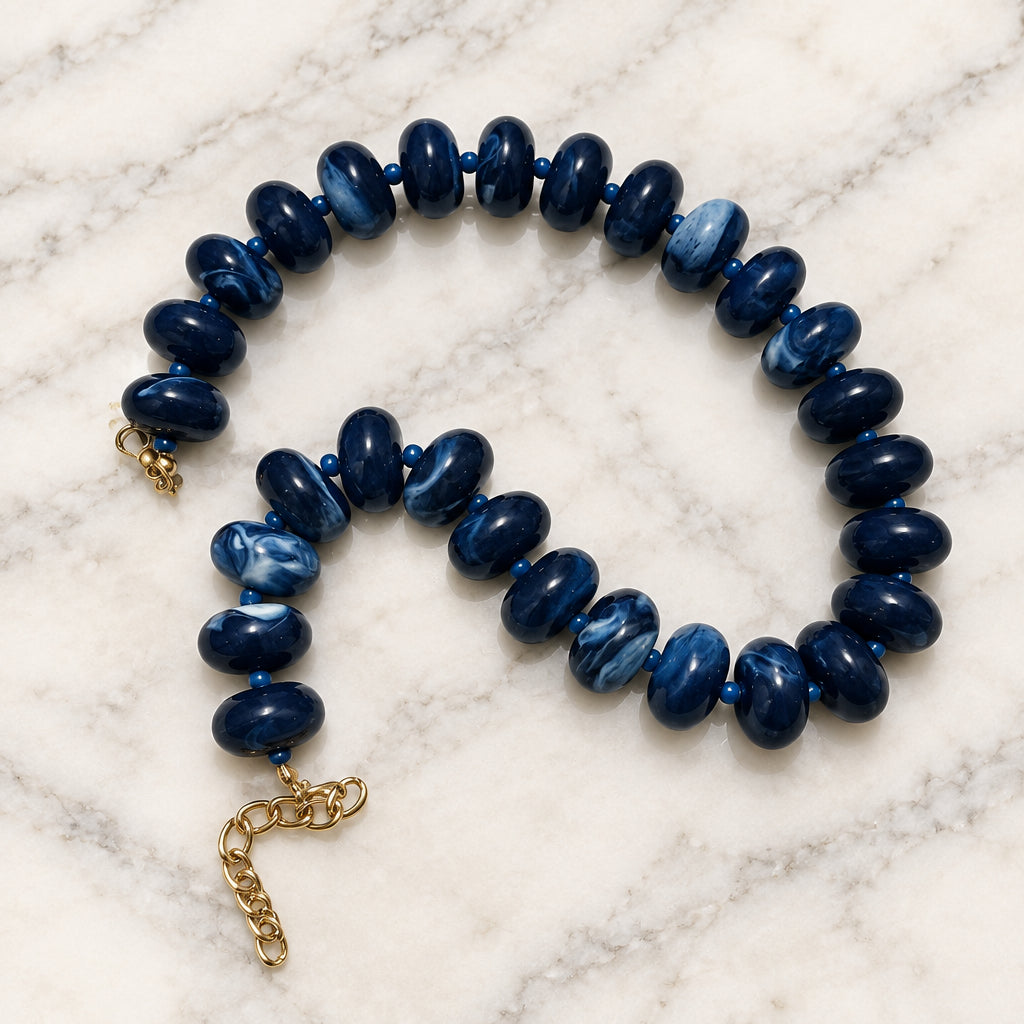 Navy marbled acrylic rondelle bead necklace with gold-tone extender chain on cream marble