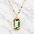 Gold-tone oval link chain necklace with a pale green emerald-cut faceted stone in a thick octagonal gold-tone frame.