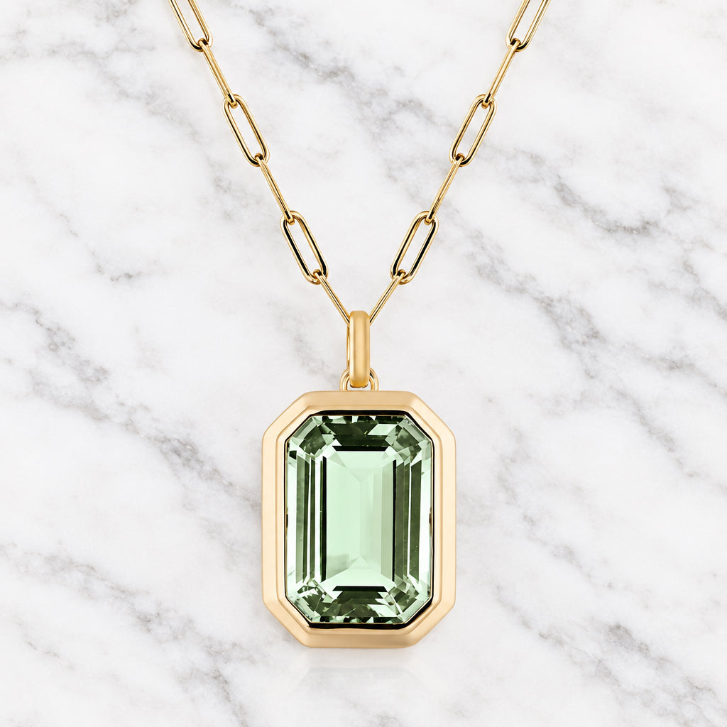 Gold-tone oval link chain necklace with a pale green emerald-cut faceted stone in a thick octagonal gold-tone frame.