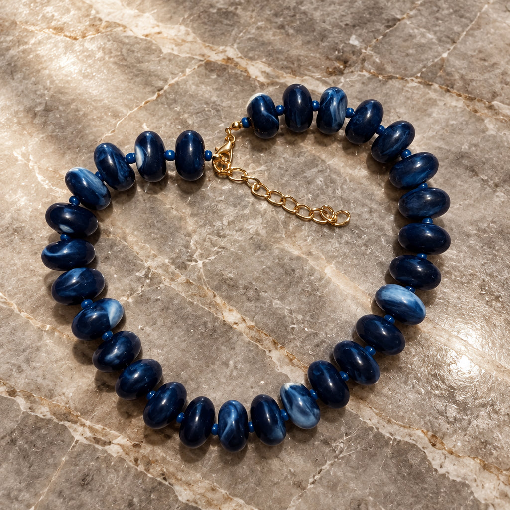Deep navy acrylic bead necklace in a loose circle on warm brown marble
