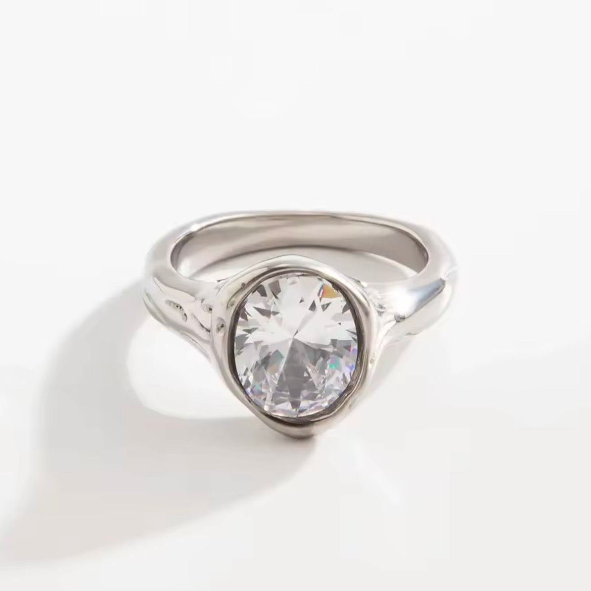 Chunky silver-tone open ring with a large oval clear faceted stone set flush in a thick border and a wavy melted texture.