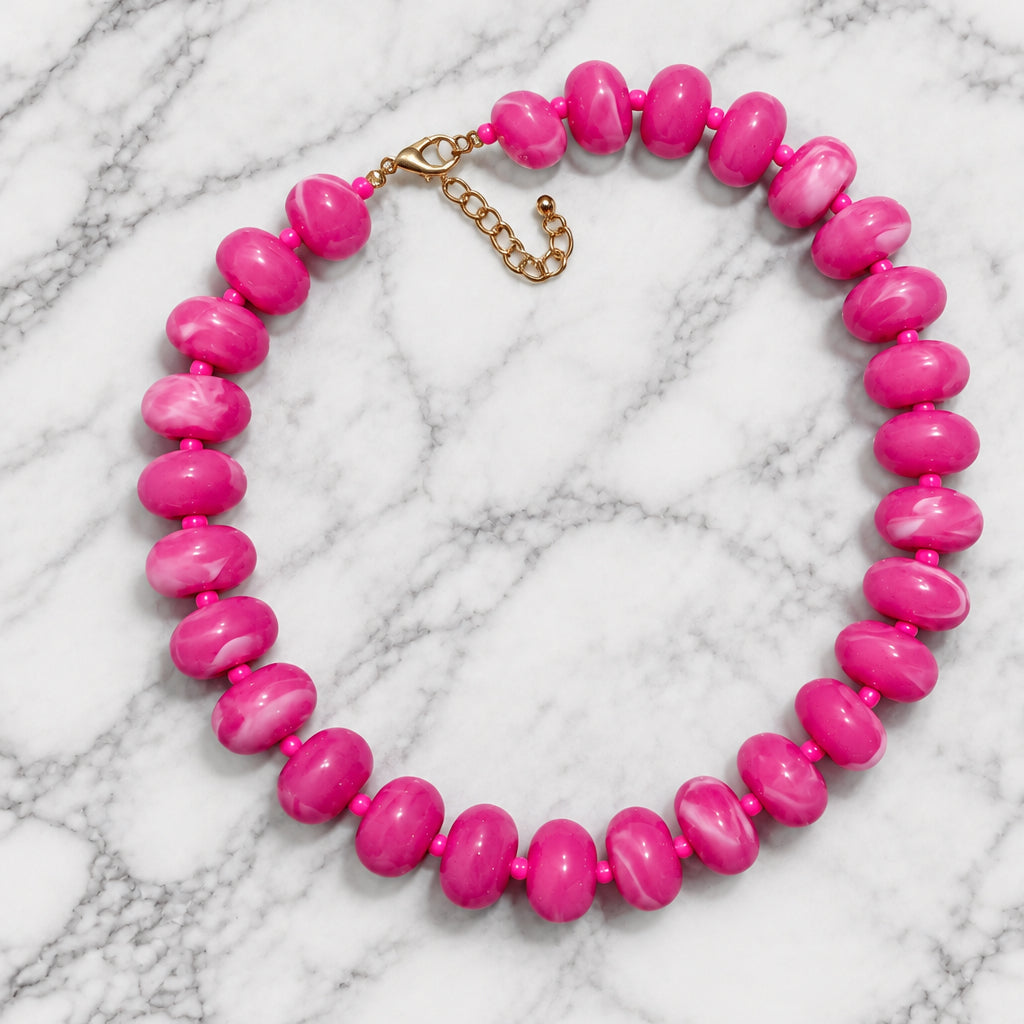 Hot pink marbled acrylic bead necklace laid in a circle on gray-veined white marble