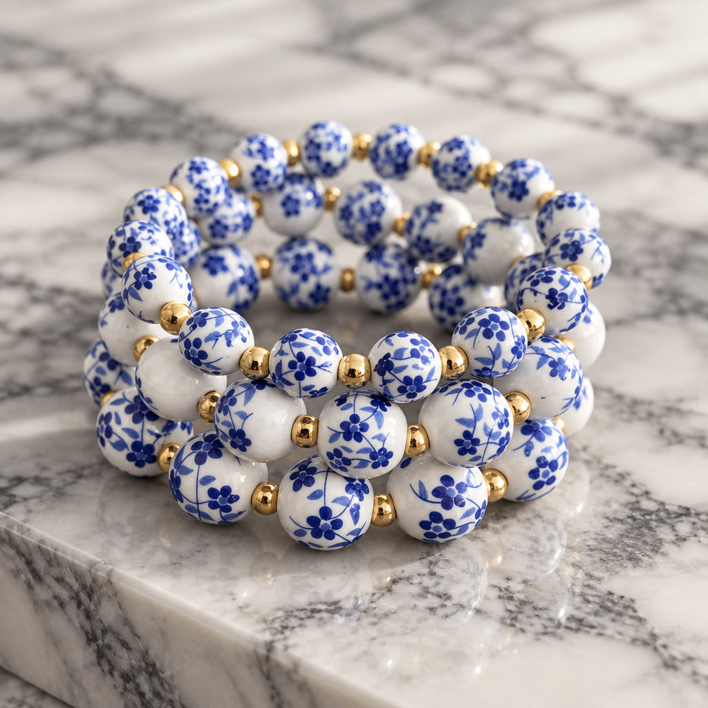 Stack of three stretch bracelets with white porcelain-style beads, dark blue floral pattern and small gold-tone spacer beads.