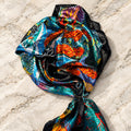 Zebra Garden Satin Scarf gathered on cream marble, showing bright teal, orange and red jungle print with black border