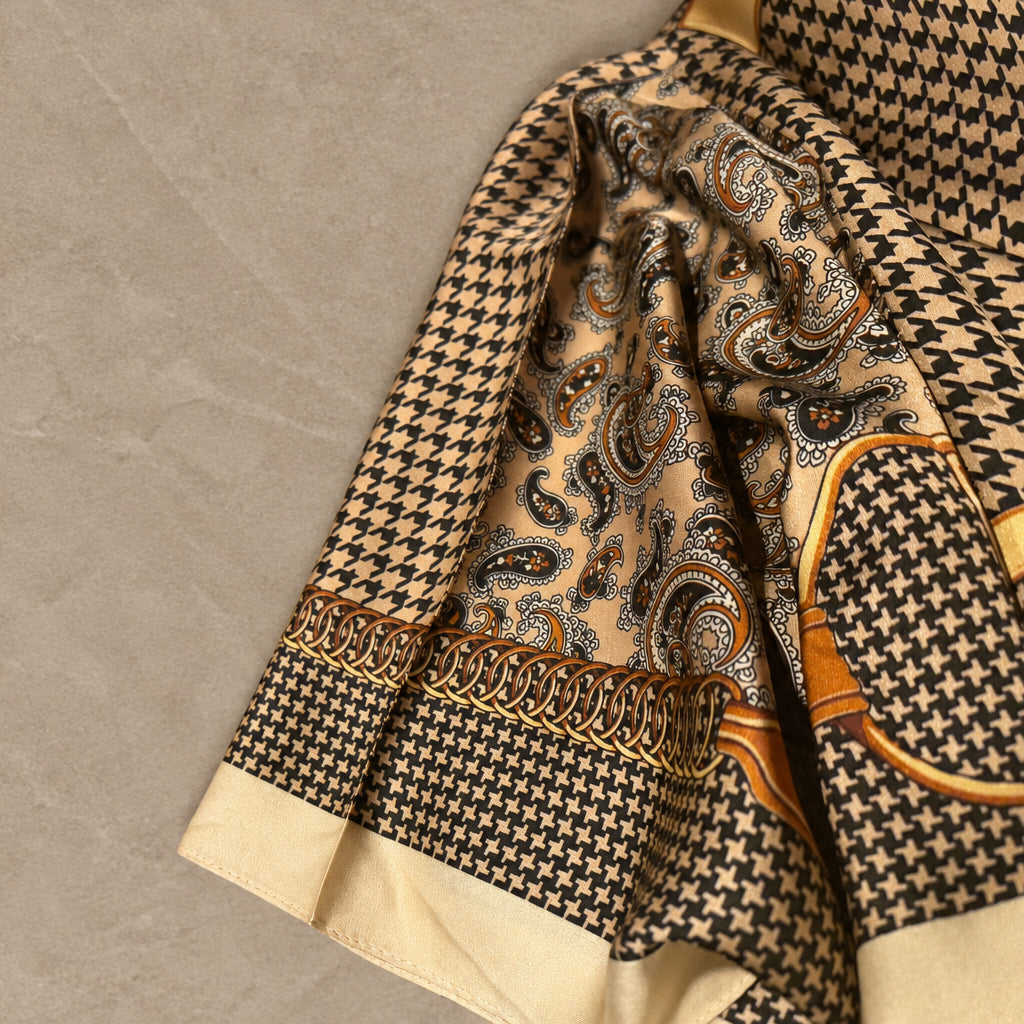 Close-up of Houndstooth Paisley satin scarf draped on gray stone, with paisley, gold chain and buckle print, cream border