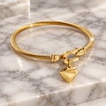 Gold-tone twisted cable bangle with a polished heart charm hanging from the clasp.