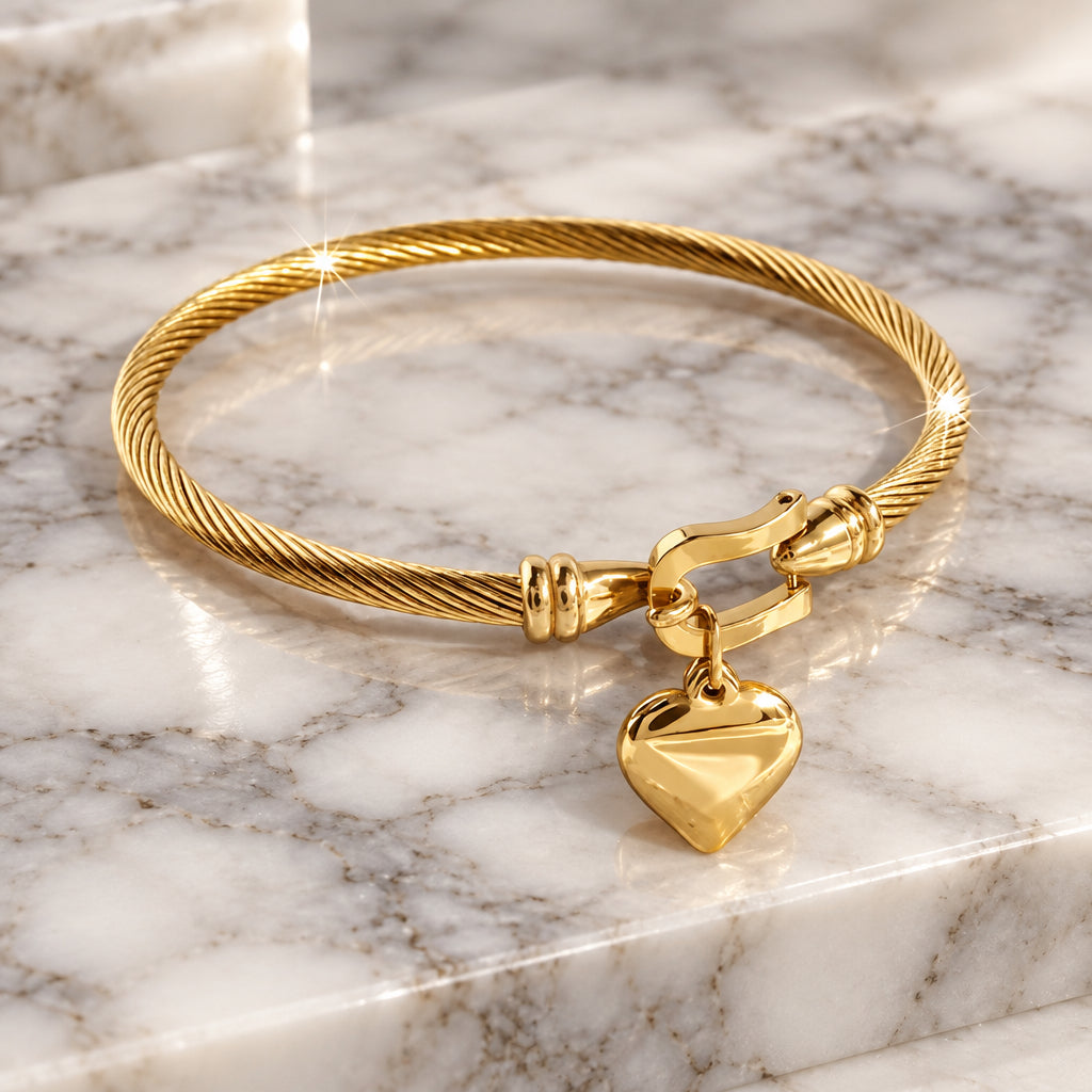 Gold-tone twisted cable bangle with a polished heart charm hanging from the clasp.