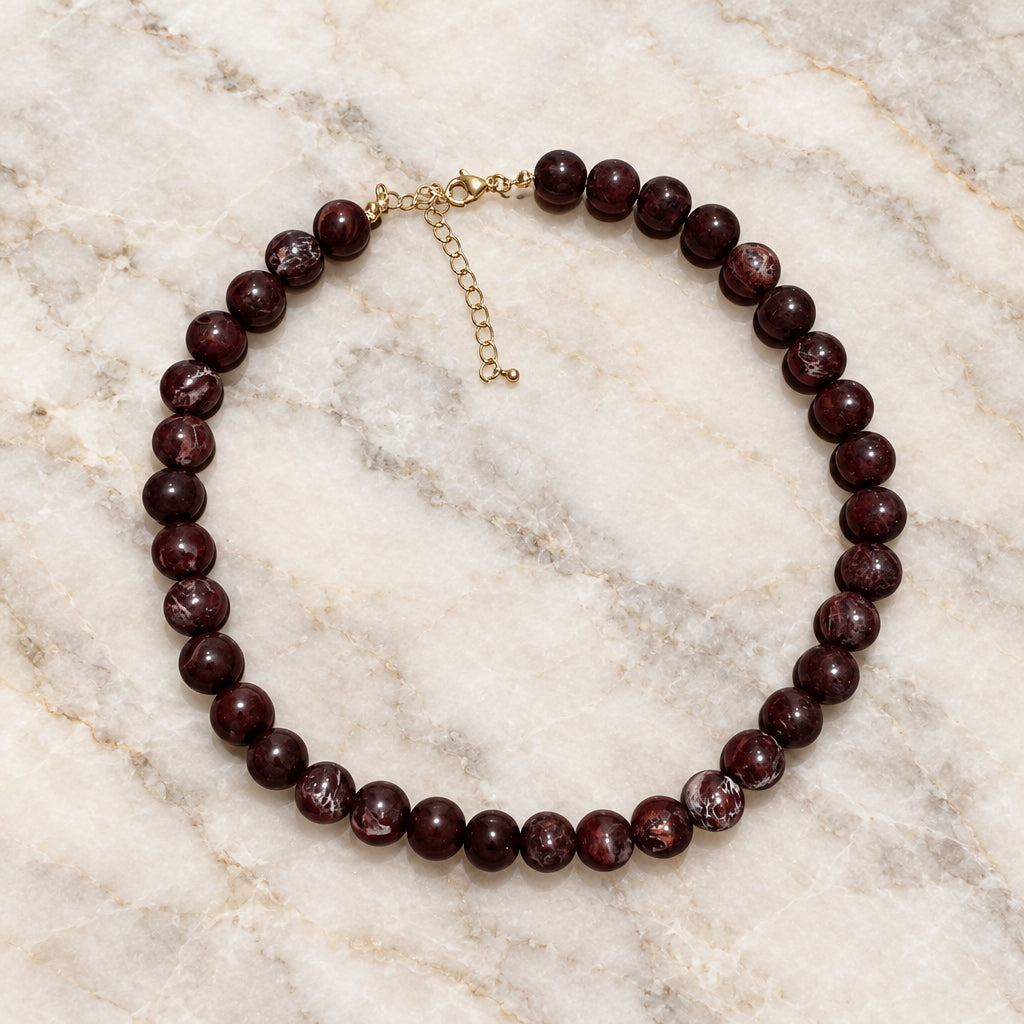 Wine-red round glossy bead necklace with gold-tone lobster clasp and extender on cream marble