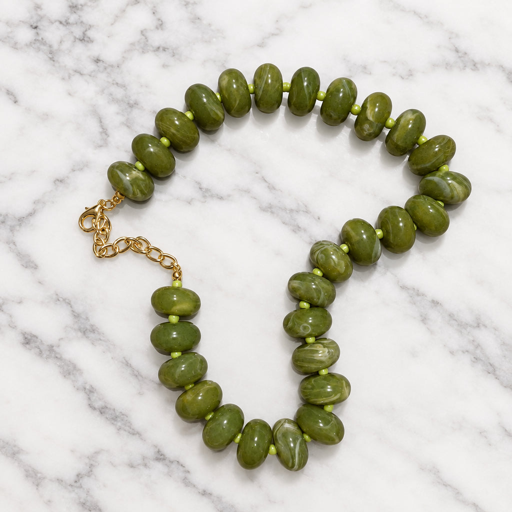 Olive green marbled acrylic bead necklace draped open with gold-tone extender on gray-veined marble