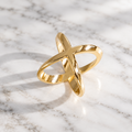 Polished gold-tone X-shaped scarf clip standing upright on marble.