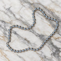 Sterling silver necklace of large polished round beads with a lobster clasp and small round tag, laid on marble.