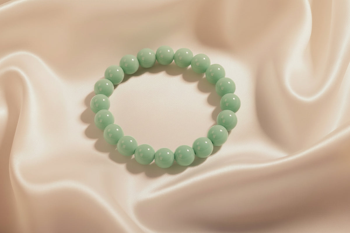 A mint green beaded bracelet with smooth, glossy round beads, displayed on a white surface next to a woven straw mat.