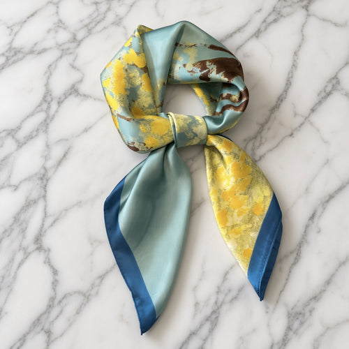 Aqua and citrine yellow satin scarf knotted with navy tips on white marble