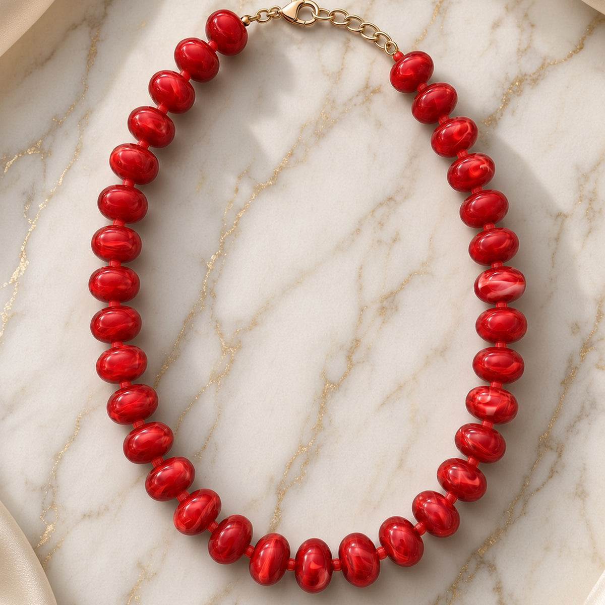 Glossy candy-apple red bead necklace with gold chain clasp on gold-veined white marble