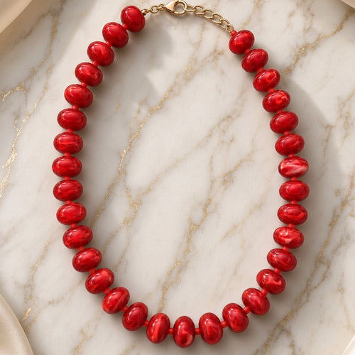 Glossy candy-apple red bead necklace with gold chain clasp on gold-veined white marble