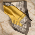 Honey and Dove satin scarf with gray paisley border, white pinstripes and a mustard yellow half, folded on cream marble