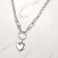 Silver-tone necklace with horseshoe links, a round ring, and a puffy heart charm on white marble.