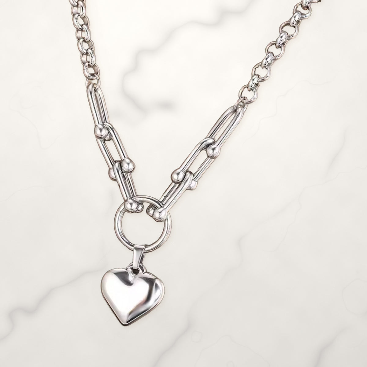 Silver-tone necklace with horseshoe links, a round ring, and a puffy heart charm on white marble.