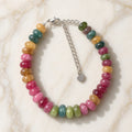 Pink, berry, green, and gold gemstone bracelet with silver heart charm on cream marble