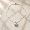 Sterling silver snake chain necklace with puffy heart pendant on gold-veined white marble