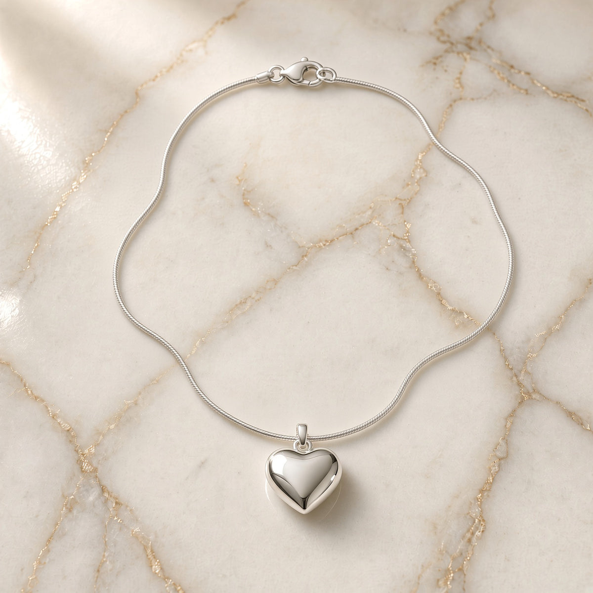 Sterling silver snake chain necklace with puffy heart pendant on gold-veined white marble