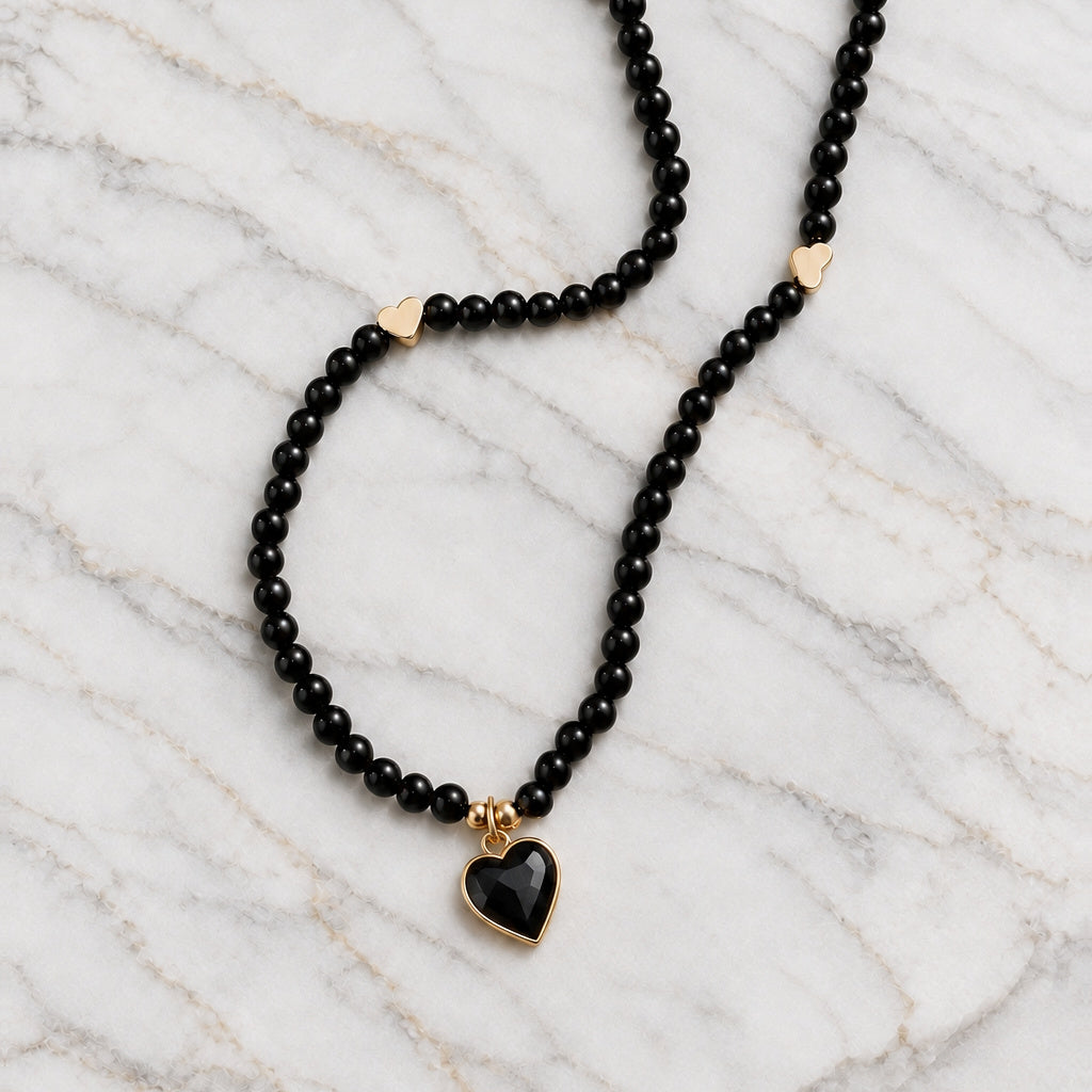 Black bead necklace with gold-tone heart spacers and black enamel heart pendant on marble