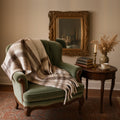 Oat and cocoa plaid blanket scarf draped over a green velvet armchair in a vintage-styled room