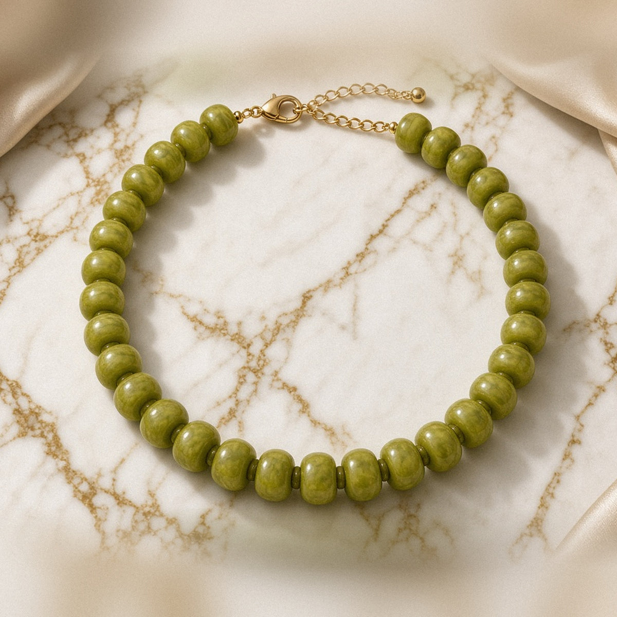 Chunky olive green acrylic bead necklace with gold-tone clasp on white and gold marble with champagne satin.