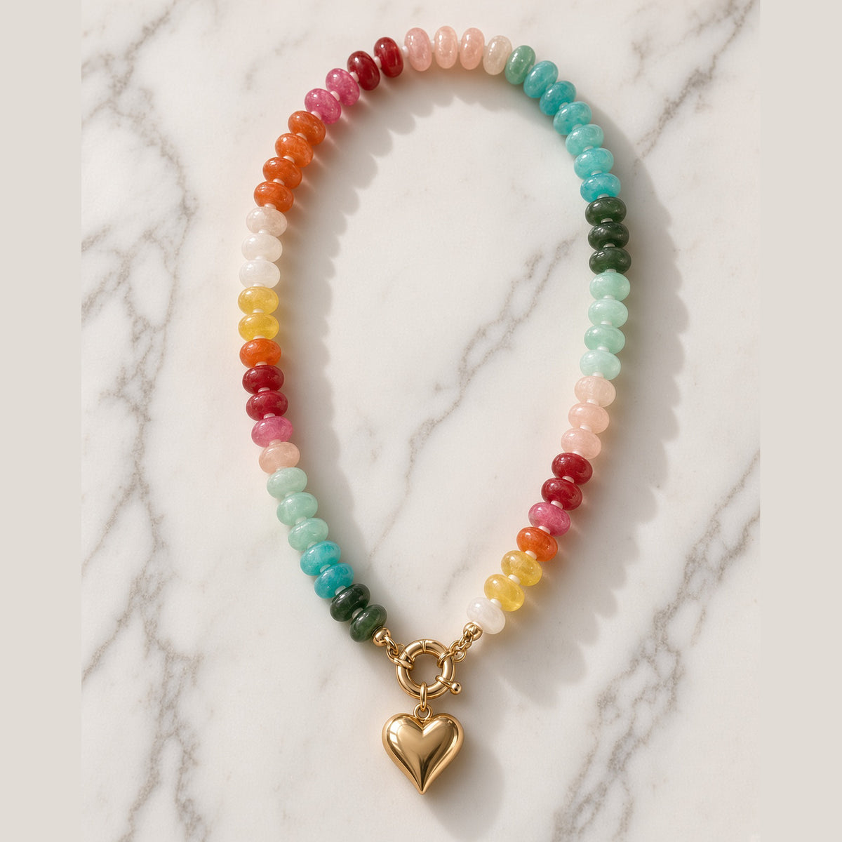 Rainbow acrylic bead necklace with gold heart charm and clasp on white marble