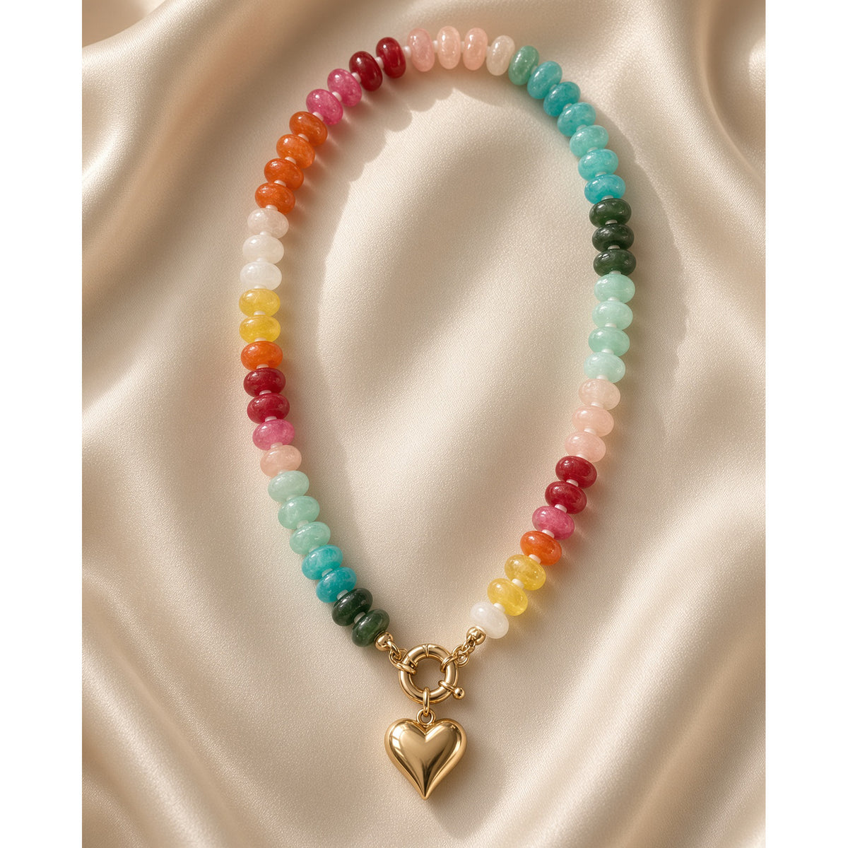 Rainbow acrylic bead necklace with gold heart charm laid on draped champagne satin