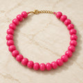 Chunky hot pink acrylic bead necklace with gold-tone clasp on white and gold marble.