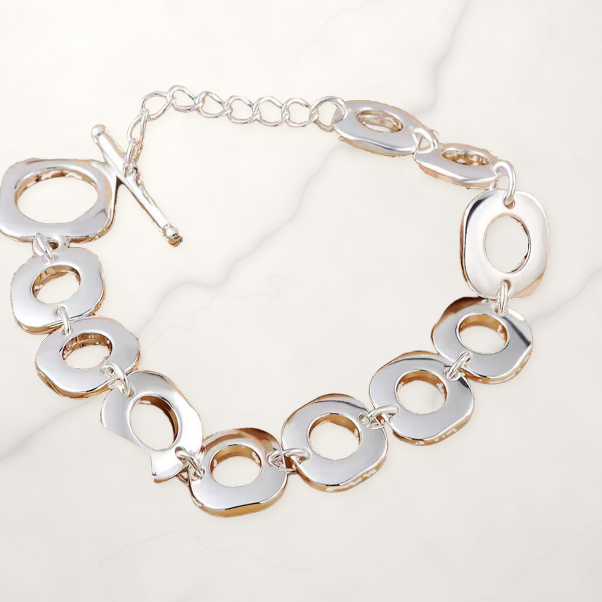 Silver-tone bracelet of rounded square open links with a toggle clasp and extender chain on white marble.