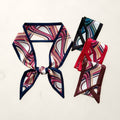 One knotted navy-bordered abstract line print twilly scarf with three folded ones in black and teal, red and burgundy on white marble.