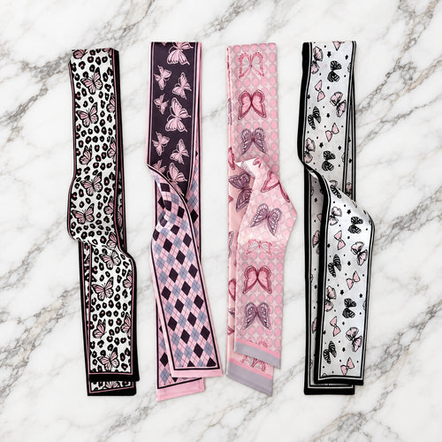 Four pink and black butterfly print twilly scarves with leopard, argyle, dot and bow accents on white marble.