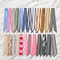 Twenty-four twilly scarves in blue, pink, neutral and black-and-white prints on white marble.