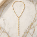 Long gold-tone Y-style lariat necklace with pearl-style beads set along the chain, laid flat on gold-veined marble.