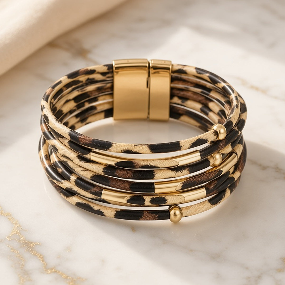 Multi-strand leopard-print wrap bracelet with gold-tone tube accents, beads and wide clasp on white marble.
