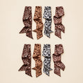 Leopard print twilly scarves in dark brown, caramel, gray and rose on white marble.