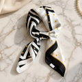 Black and white striped satin square scarf with mustard polka dots and black border, tied in a soft knot on gold-veined marble.