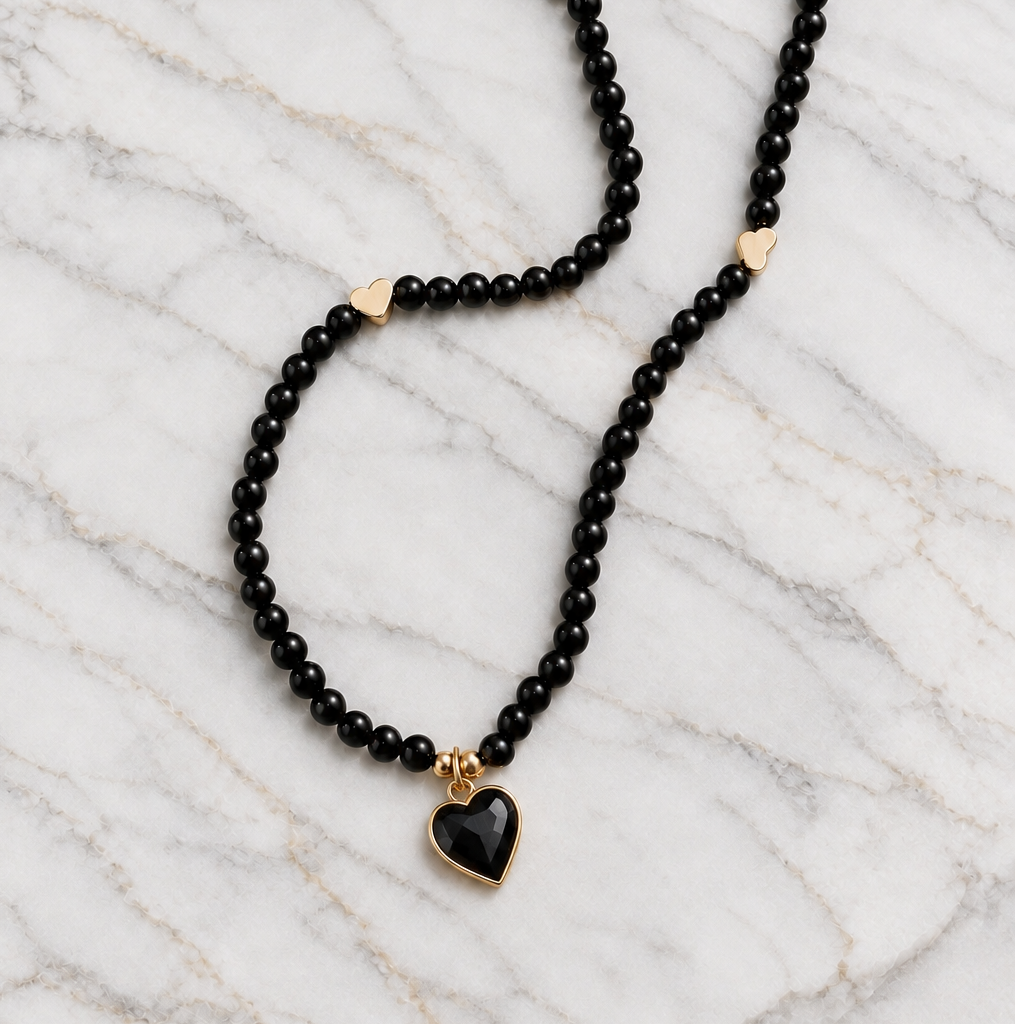 Black bead necklace with gold-tone heart spacers and black enamel heart pendant on marble