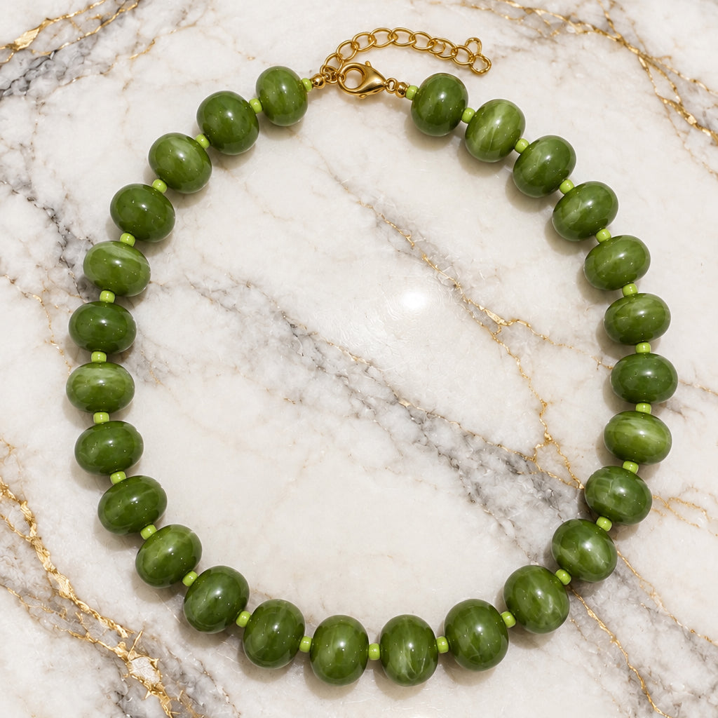 Olive green acrylic rondelle bead necklace with gold-tone clasp on gold-veined white marble