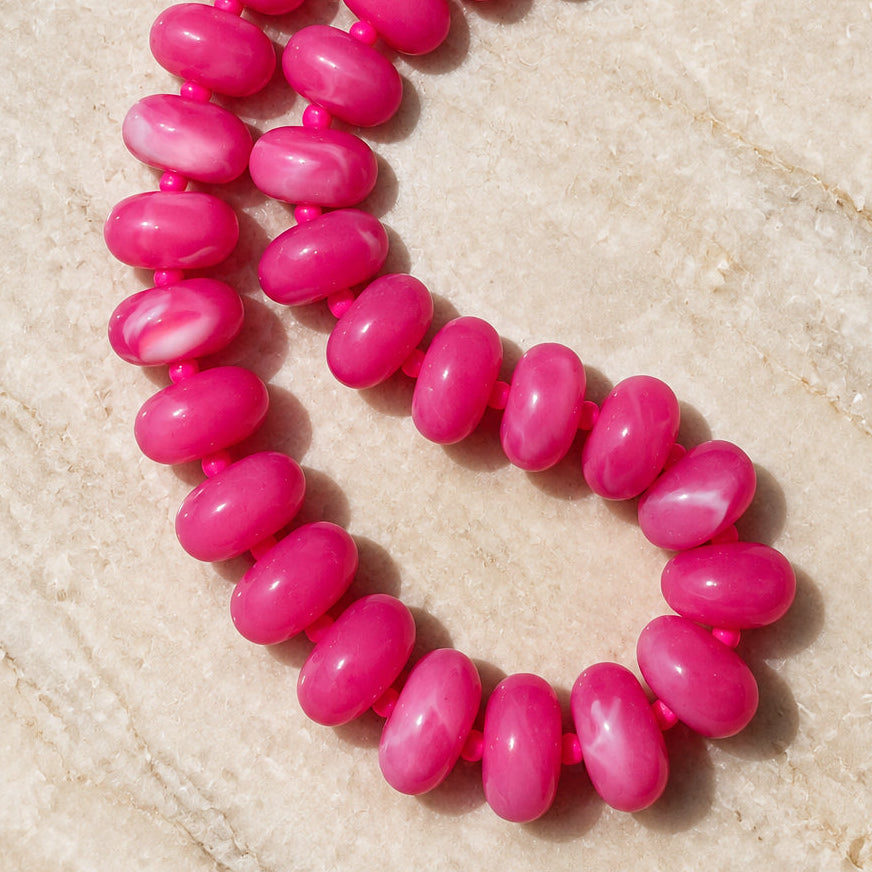Hot pink acrylic rondelle bead necklace with gold-tone clasp on sunlit cream stone
