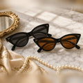 Riviera cat-eye sunglasses in gray and brown lenses on a marble vanity with pearls