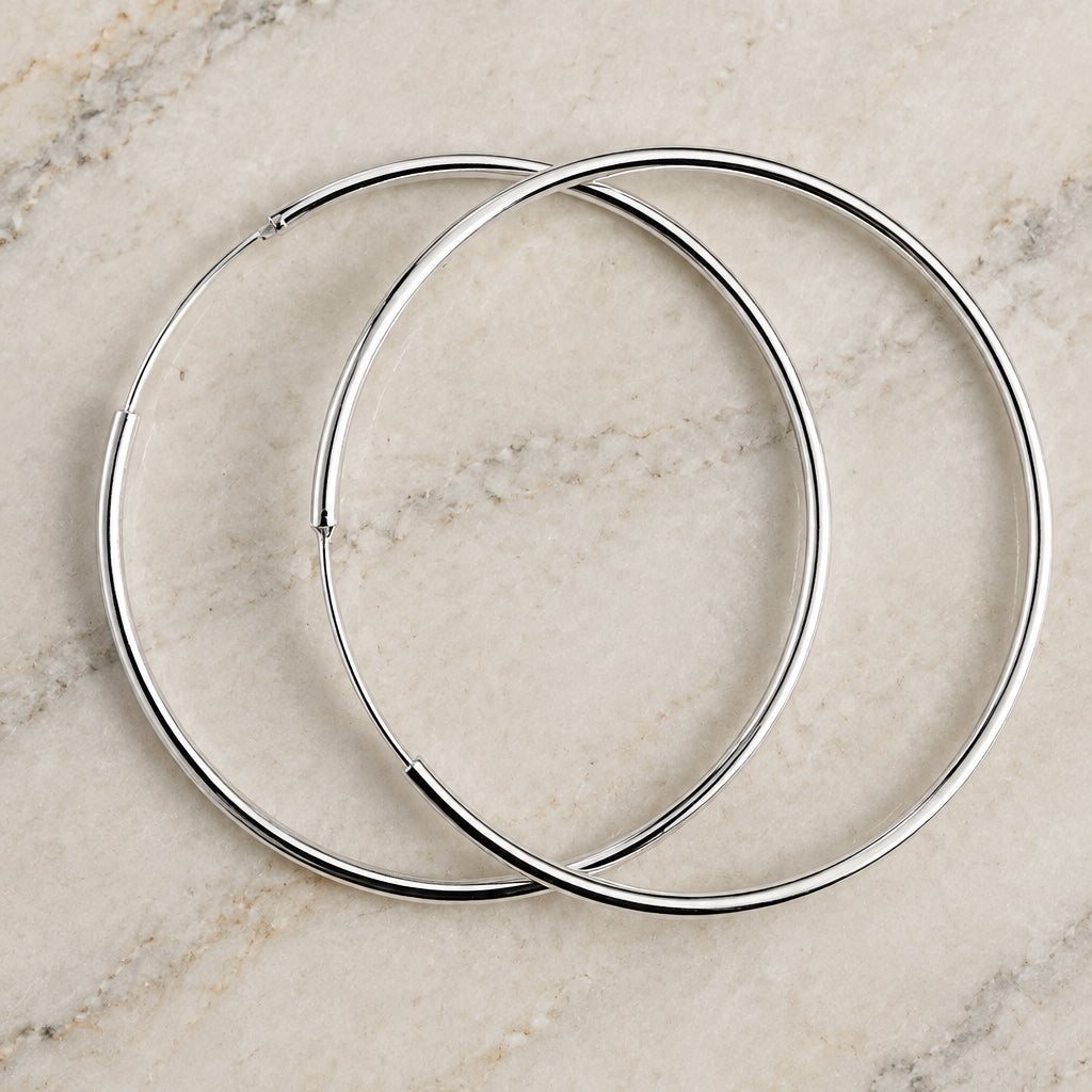 Large 925 sterling silver hoop earrings overlapping on cream marble