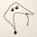 Gold chain necklace with a brown stone oval pendant and matching stud earrings on cream marble.