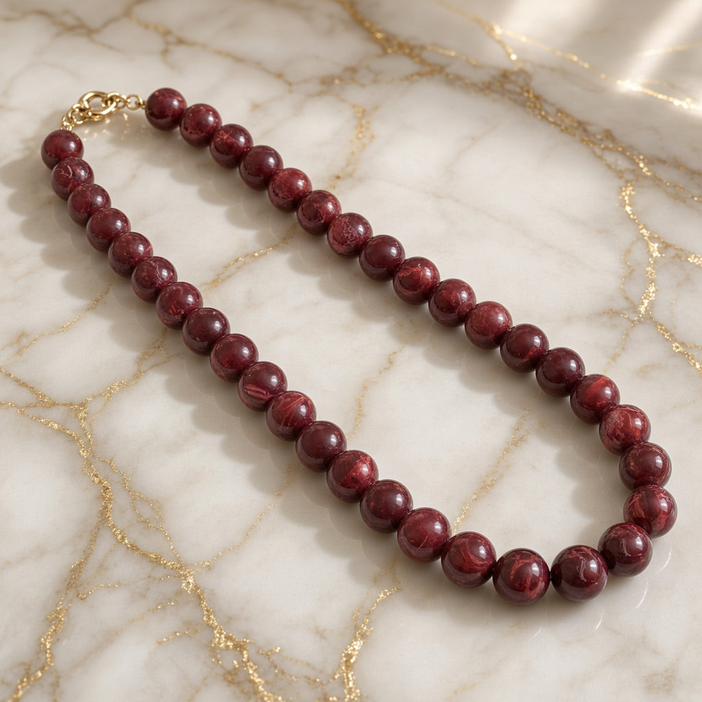 Burgundy swirled bead necklace with gold-tone clasp on white marble with gold veins